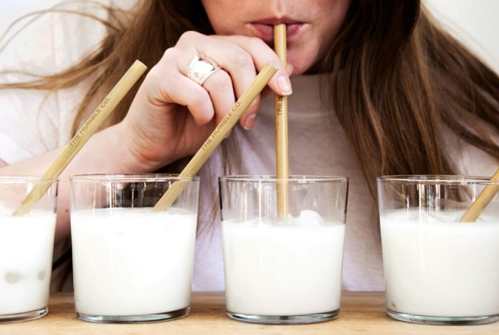 複数のグラスに注がれた牛乳をストローで飲む女性の写真