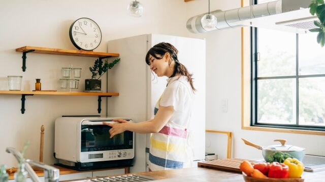 キッチンで電子レンジを開けようとsする女性の画像