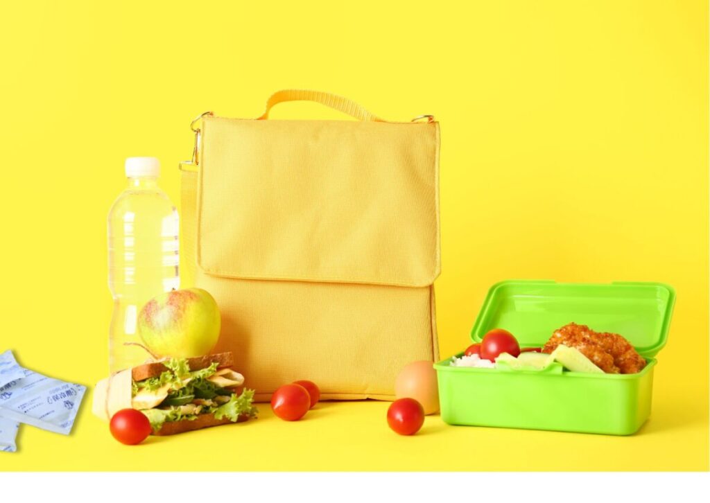 黄色のお弁当袋の前に、緑色のお弁当箱にはいったお弁当とサンドイッチが置いてある画像